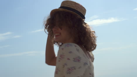 mujer riendo girando rebotando en el agua de mar sosteniendo un sombrero de paja de cerca.