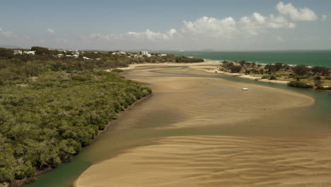 Aerial-trucking-shot-showing-sandy-river-with-water-spots-and-Pacific-Ocean-in-background-during-sunny-day