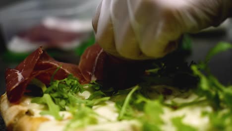 preparing a gourmet pizza with smoked meat and arugula