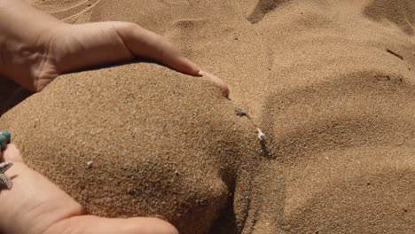 manos de mujer acariciando la arena y tirándola de vuelta a la playa