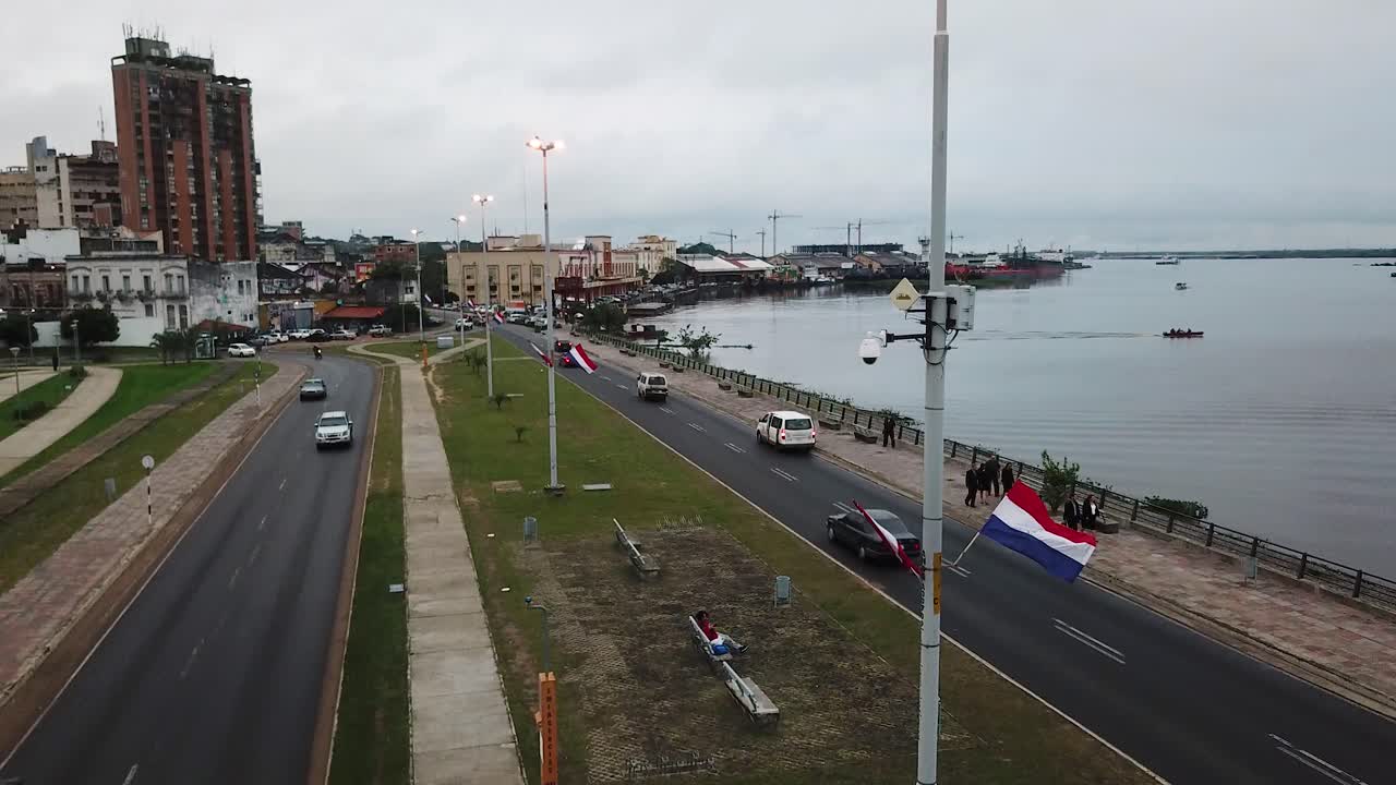 Paraguayan flag waving in the wind on costanera avenue, with the paraguay river and the city of asuncion in the background