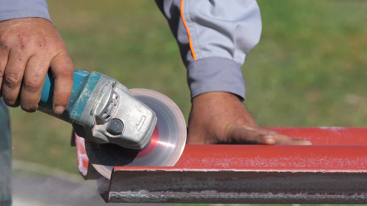 primer plano de un hombre con ropa de trabajo cortando una lista de techos de acero rojo por sierra de corte de metal. clip. materiales y equipos para el hogar