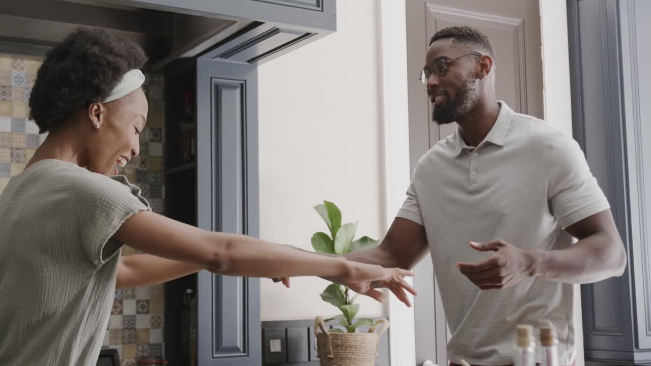 Happy african american couple holding hands and dancing in ktichen in slow motion