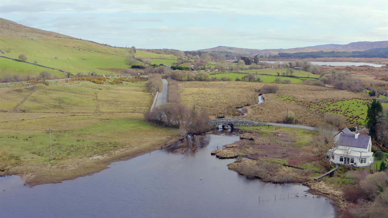 Aerial pullback and ascent from the famous stonework of the Quiet Man Bridge against Connemara's scenic landscape.