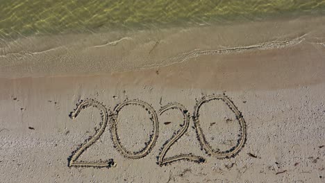 static shot of twenty twenty written in the sand as water laps onto the beach