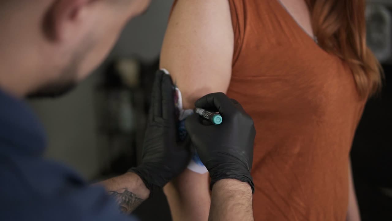 Young bearded tattooer drawing sketch on the arm of his client's female hand, contouring sketch with felt tip pen. Starting of a process. Close up
