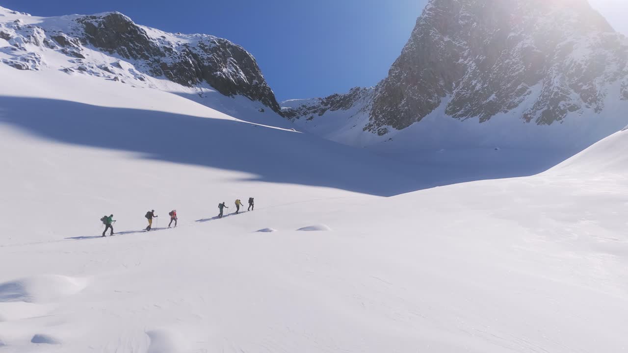 Aerial revealing shot showing group of mountaineer hiking uphill snowy mountains in sunlight
