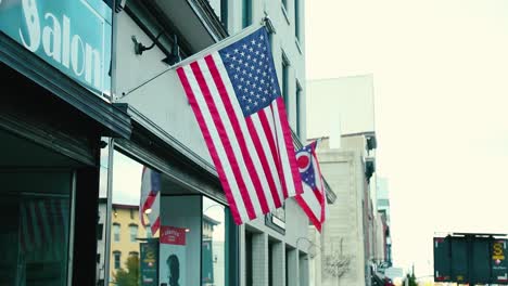 us and ohio american flags hang in the bresze in front of a small business over the sidewalk in a small quaint town