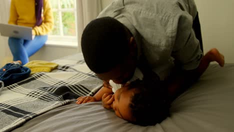 Front-view-of-black-father-helping-his-son-changing-his-clothes-on-bed-in-a-comfortable-home-4k