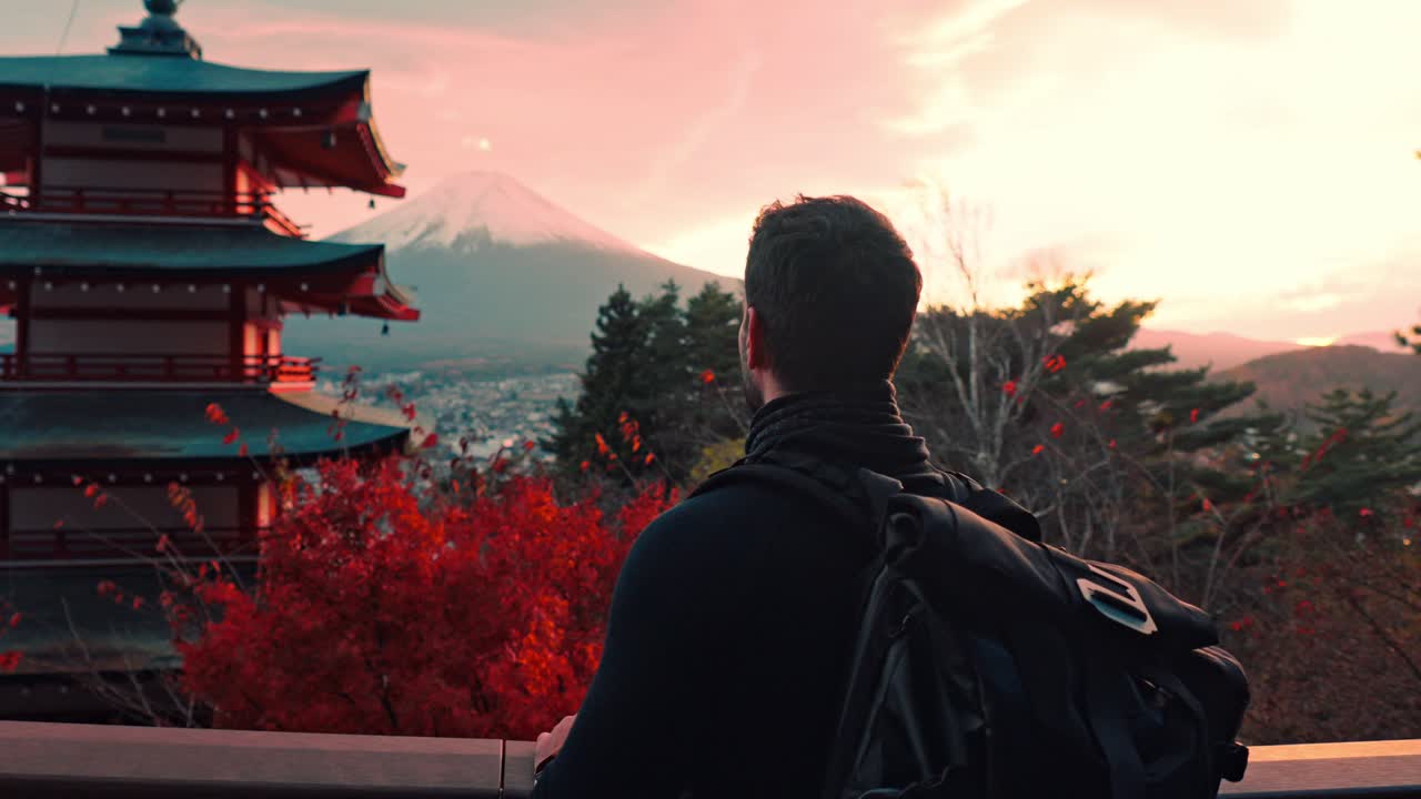 un hombre admira la impresionante vista de la pagoda chureito durante la puesta de sol, con el monte fuji de pie en el fondo.