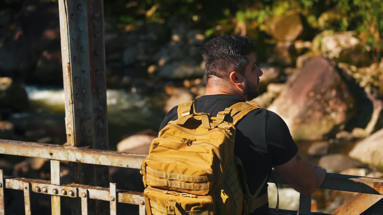 Young caucasian traveler with backpack looking into the nature on rusty old bridge outdoors on sunny summer day