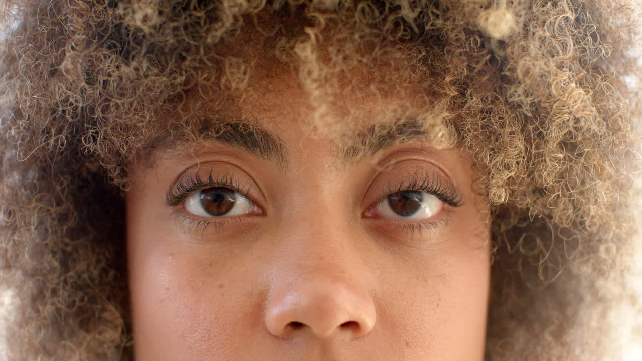 A biracial young woman with curly hair and brown eyes is looking forward