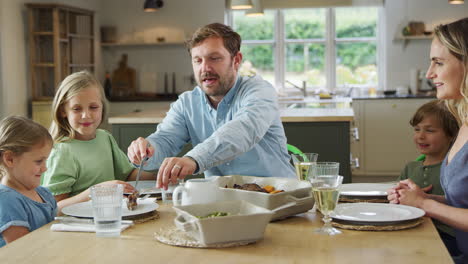 Vater-Serviert-Essen,-Während-Die-Familie-Zu-Hause-Am-Tisch-Sitzt-Und-Gemeinsam-Das-Essen-Genießt