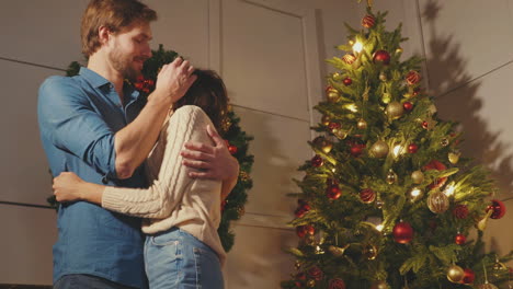 una pareja abrazándose junto al árbol de navidad.