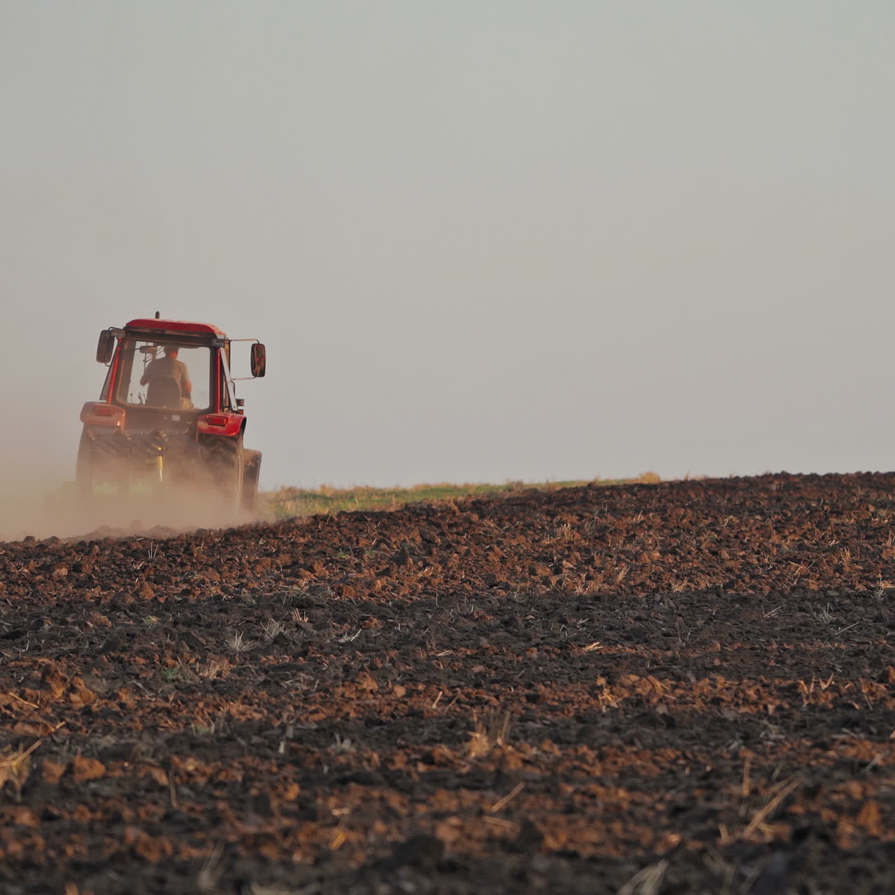 Brown field background and a tractor plowing the soil. Tractor cultivating the field, preparing land for sowing in the farmland.