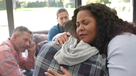 Two-diverse-male-and-female-friends-hugging-in-group-therapy-session