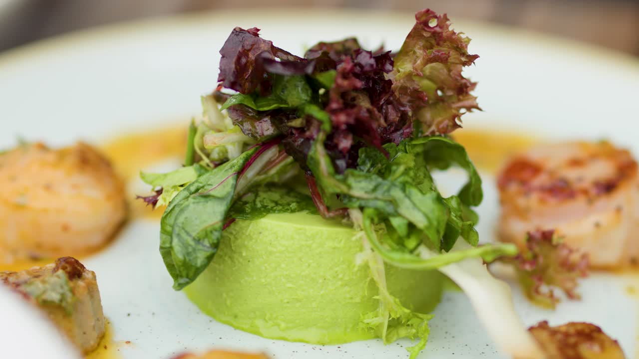 Gourmet green pea panna cotta plated with scallops, microgreens, and vibrant salad under soft lighting