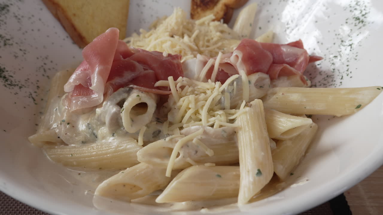 Una ciotola di fettuccine con formaggio grattugiato, pezzetti di prosciutto ed erbe fresche.