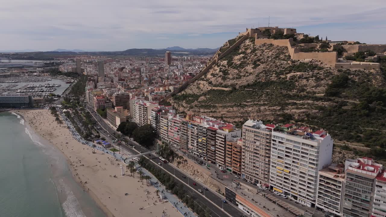 Drohnenaufnahme von Alicantes Küstenlinie mit Playa del Postiguet, der Stadtskyline und der Burg Santa Bárbara auf dem Berg Benacantil. Mittelmeerstrand und Uferpromenade entlang der Costa Blanca in Spanien.