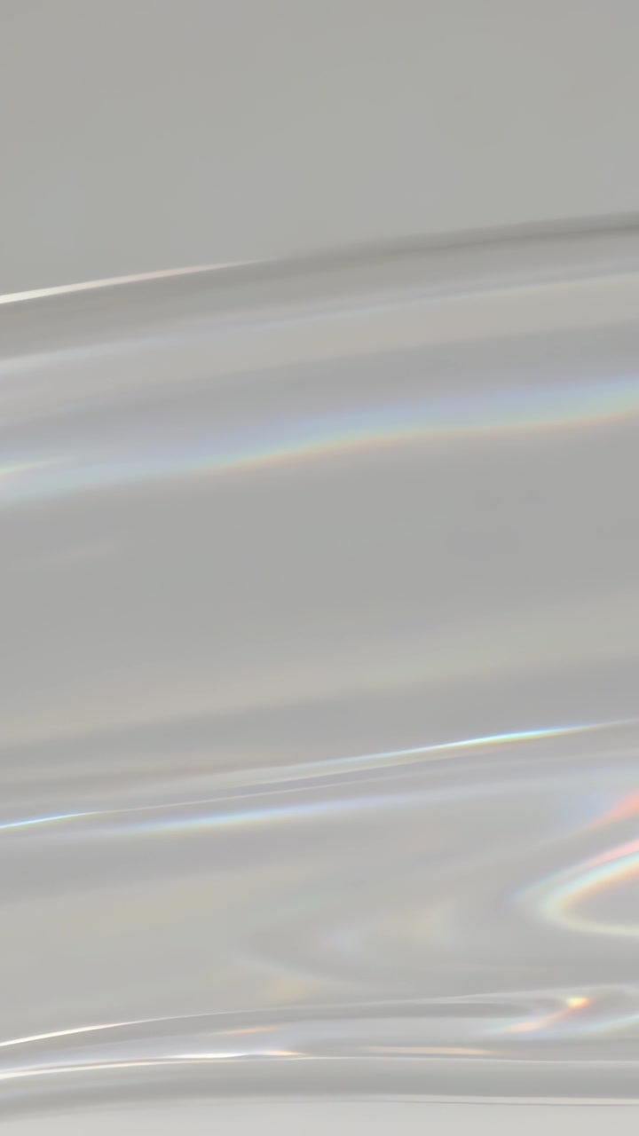 Vertical video: Shifting translucent iridescent film rippling rainbow bands in studio, light moving
