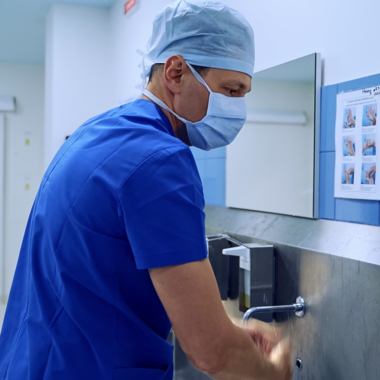 Médico do sexo masculino de uniforme azul, máscara e touca lavando as mãos cuidadosamente. Cirurgião se preparando para a operação na sala pré-operatória. Esterilidade na cirurgia