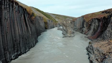 aerial down glacial river with dramatic basalt rock columns, studlagil, iceland