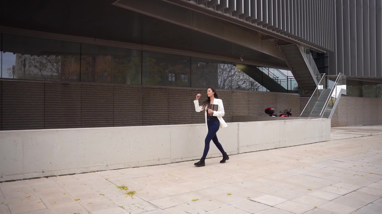 A woman confidently walks in the vicinity of modern architecture amidst an urban setting
