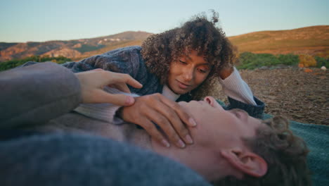 curly lady touching boyfriend cheek resting sundown hill closeup. pair cuddling