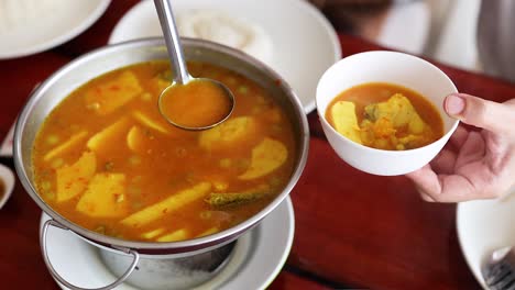 ladle serves yellow curry into a bowl