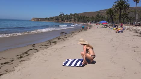 una mujer con sombrero de paja yace al sol en una playa de california