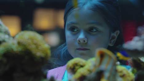 happy girl in aquarium looking at fish curious child watching colorful marine life swimming in tank learning about sea animals in underwater ecosystem inquisitive kid at oceanarium