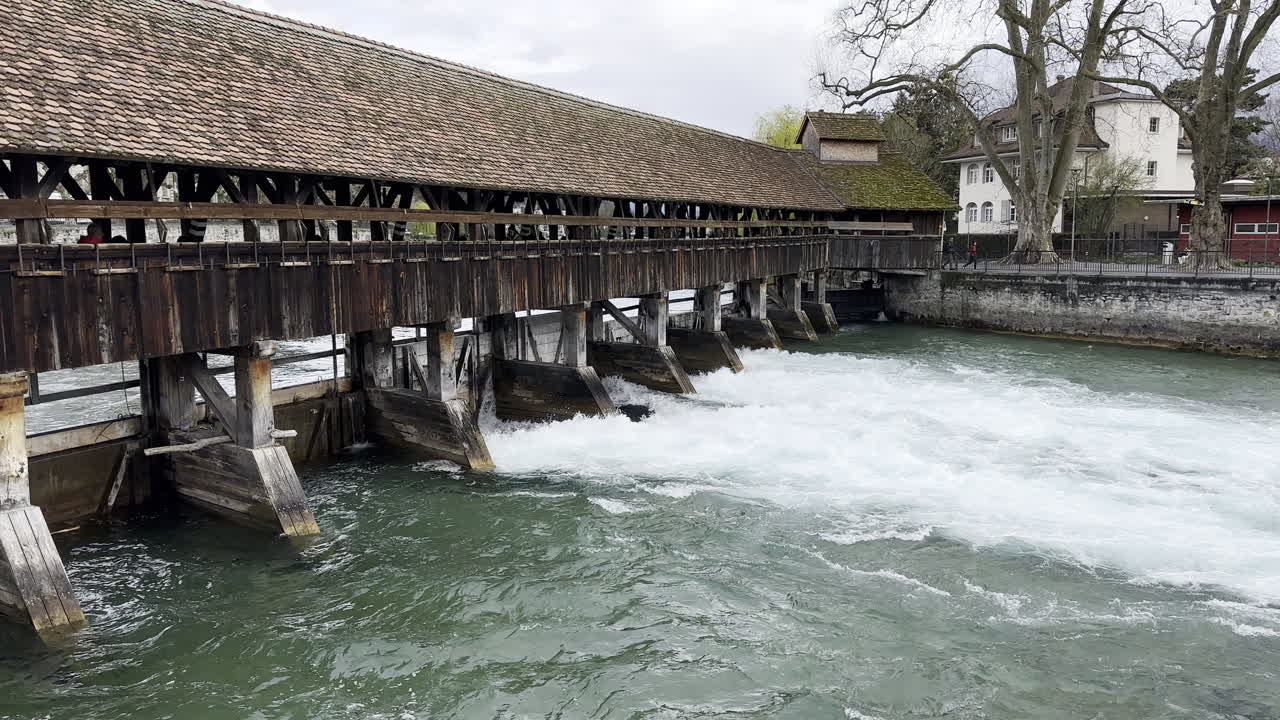 Stream flowing forcefully under a wooden bridge with a dam