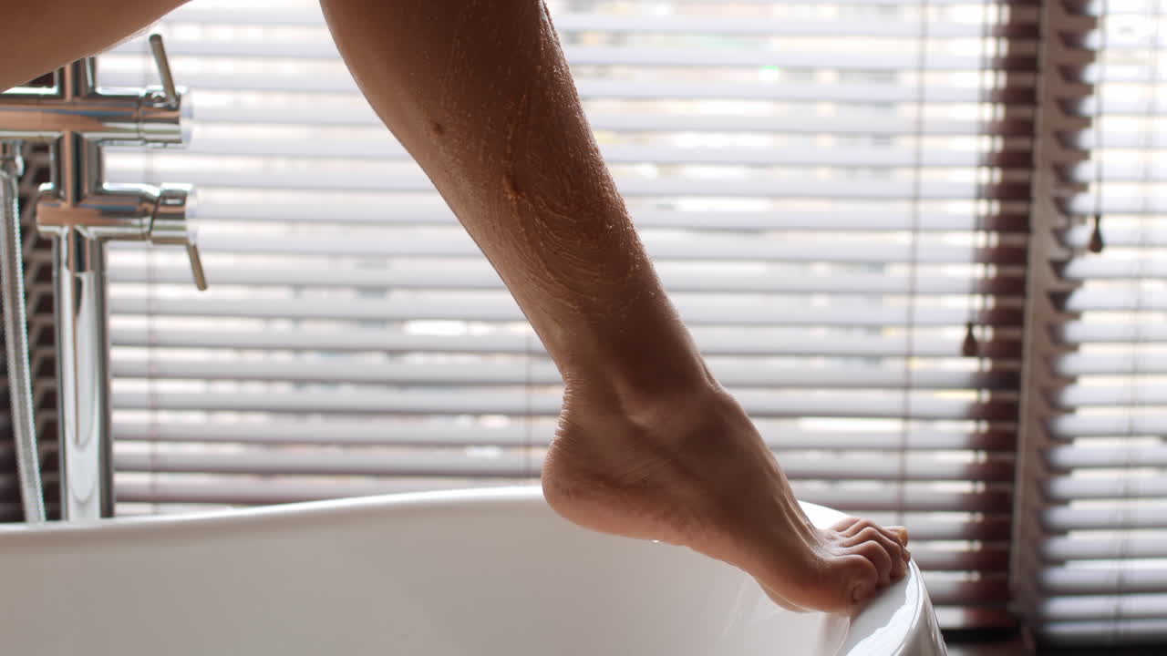 Woman Scrubbing Her Legs in a Bathtub