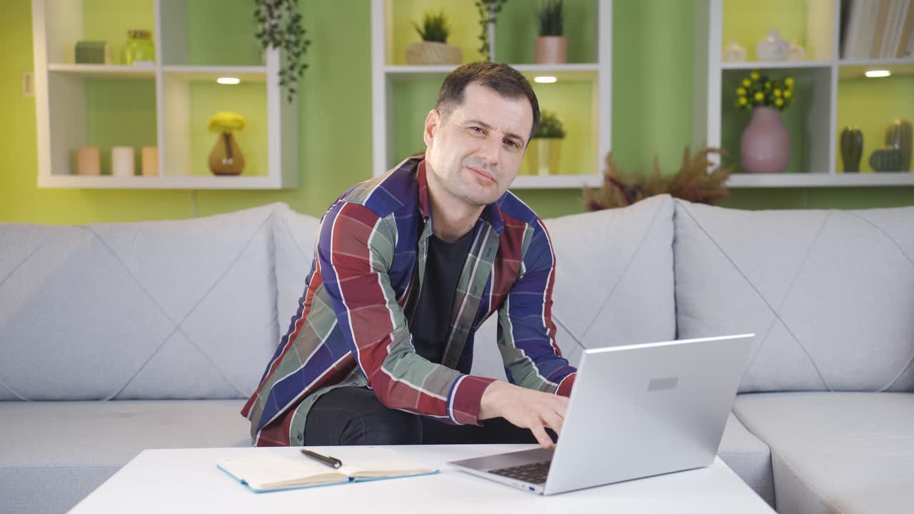 hombre sonriendo a la cámara mientras trabaja en la computadora portátil.