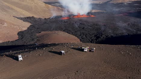 jeeps parked on hill edge overlooking meradalir valley with fissure volcano eruption, aerial