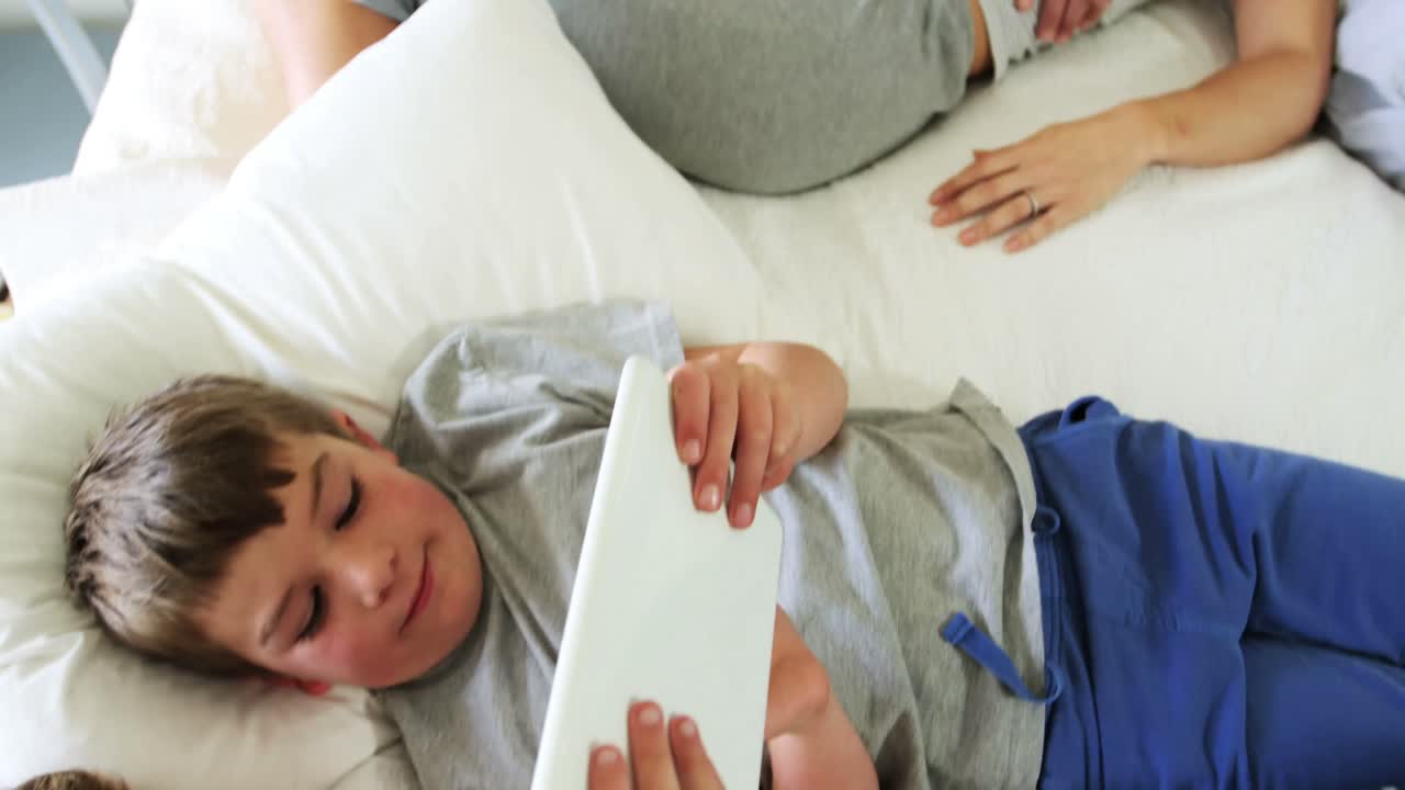 hermanos usando tableta digital mientras los padres duermen en el dormitorio 4k