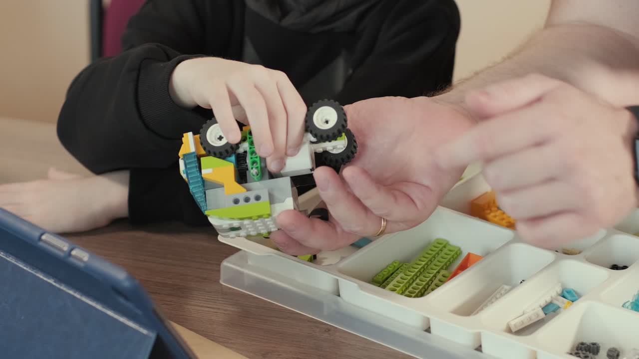 дети внимательно сосредоточились на сборке частей из робототехнического набора, с планшетом, отображающим инструкции, способствуя обучению и творчеству.