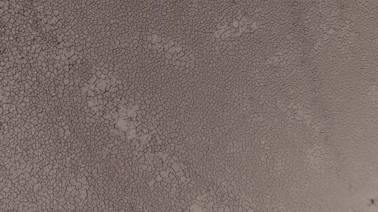 A close-up drone view of extensively cracked, dry earth creates a detailed natural texture across the entire frame.