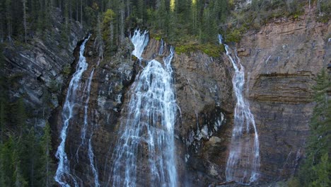 drone flying backwards revealing a huge waterfall surrounded by woods in canmore, alberta