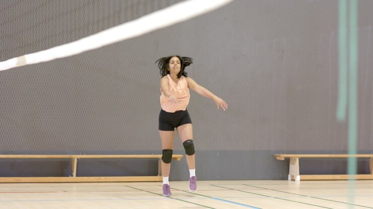 Female athlete bumping, passing, spiking ball after partner tossing over net in gym, copy space
