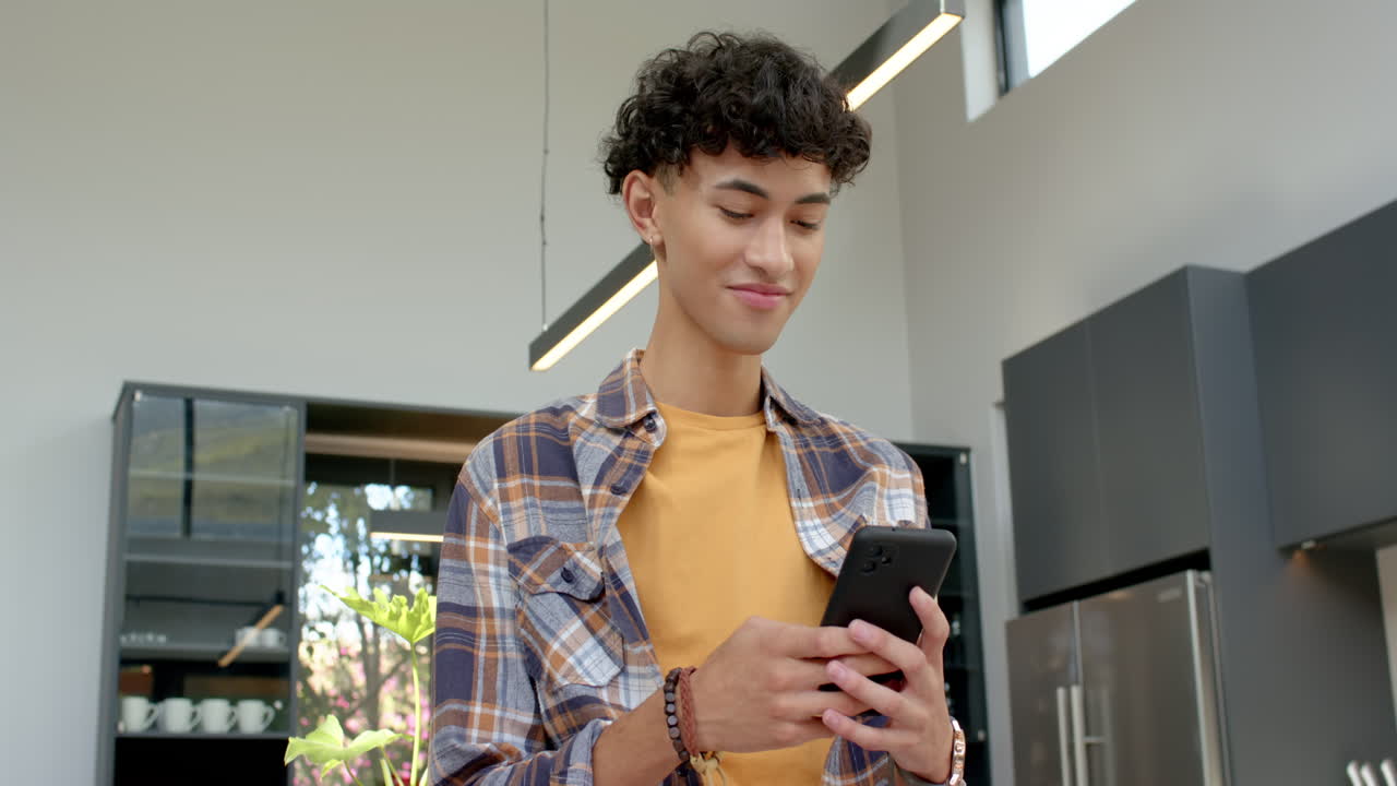 Using smartphone, teenage boy smiling and standing in modern kitchen