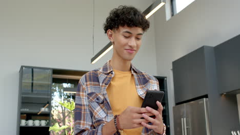 using smartphone, teenage boy smiling and standing in modern kitchen