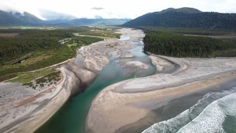 aerial view of mahitahi river in new zealand, winding through sandy banks and dense forest on shoreline