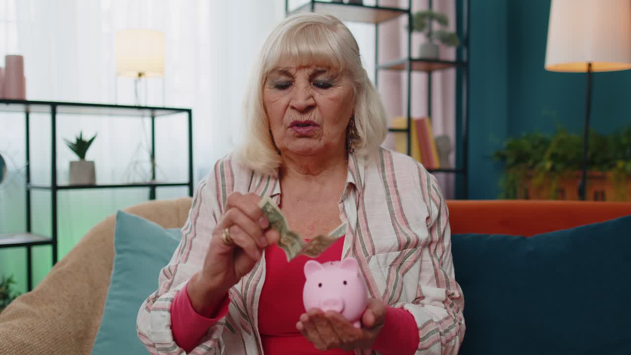 Sad poor senior old woman counting money from piggybank holding last one dollar cash poverty debt
