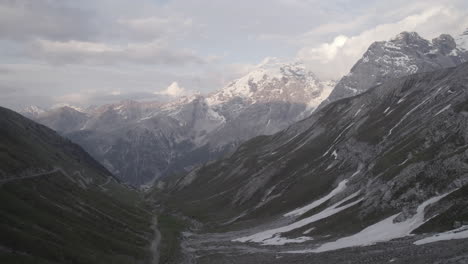 Drone-shot-flying-over-the-Stelvio-Pass-Italy-on-a-grey-day-going-to-the-scenic-view-of-the-snowy-mountains-in-the-background-on-a-grey-day-during-sunset-time-LOG