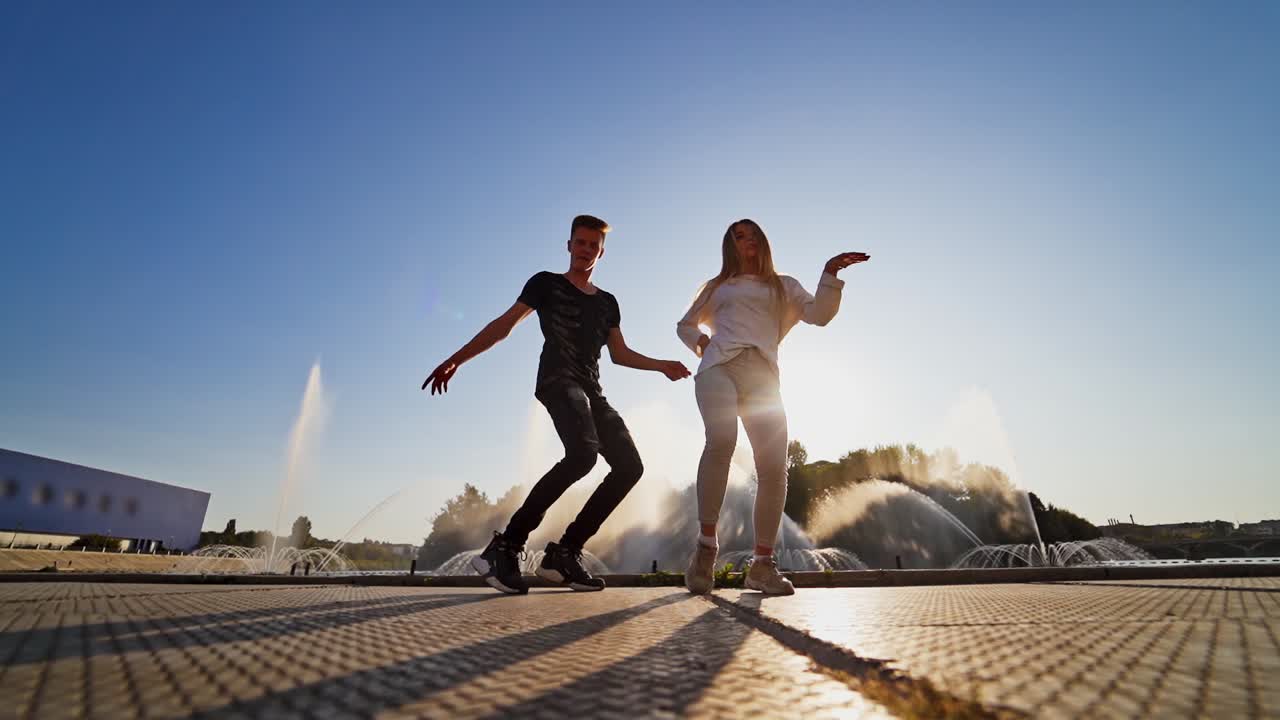 Dancers against beautiful fountain. Young couple performing a modern dance on the urban background. Contemporary freestyle dance of teens outdoors through the leaks of sun.