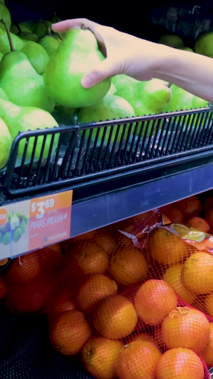Un acquirente seleziona pere fresche da un vivace espositore di prodotti freschi in un supermercato di Melbourne, mostrando la spesa quotidiana
