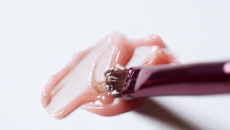 mixing different shades of lip balm colours using a small brush applicator on a clean white board palette