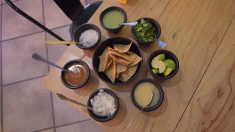 red, yellow, green salsa with onions, cilantro, limes, tortilla chips on table