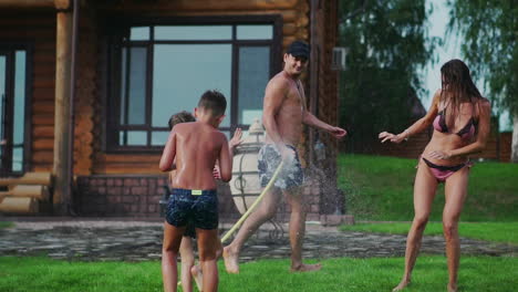 family in the backyard of a country house in the summer relax playing with water and hosing
